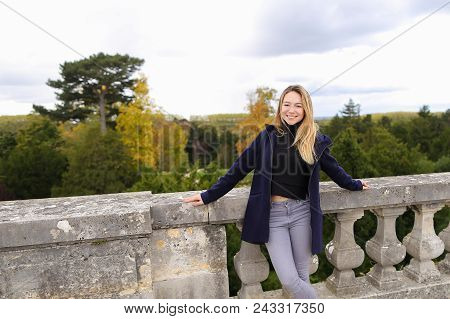 Girl Standing Near Concrete Railing With Green Trees Background. Concept Of Architectural Elements A