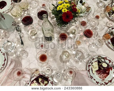 After A Long And Elegant Dinner, A Table With White Tablecloth Is Full Of Empty And Half-empty Wine 