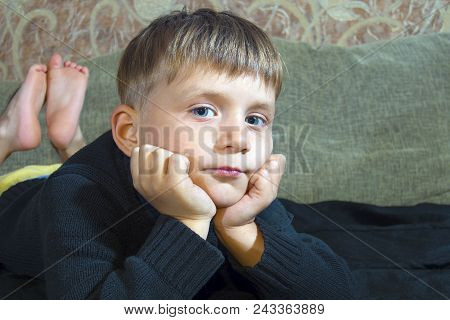 Little Boy Is Lying On The Couch And Is Looking At The Camera