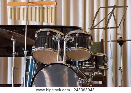 A Drum Set On A Black Piano Background In A Concert Hall.