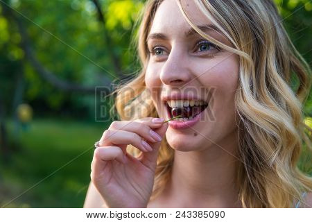 Girl Eating Cherries In Outdoor Park. Green Background