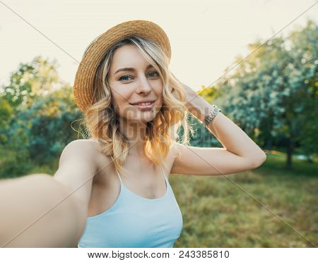 Stylish Modern Girl Taking A Selfie Out In The Park. She Is Wearing Hat