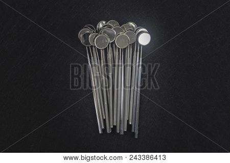 Stack Of Dental Mirrors On The Center Of Dark Background. Top View
