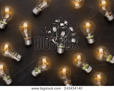 One Broken Light Bulb Among Whole Glowing Ones On Black Background, Top View. Creativity, Idea And F