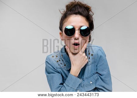 Young Girl In Round Glasses On A Gray Background. Portrait Of A Young Beautiful Girl. Charming Girl 