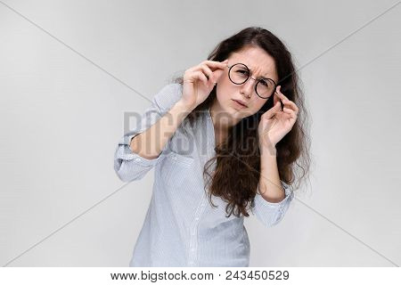 A Young Girl In A Light Blouse And Dark Trousers. The Girl Looks At Herself In The Mirror.