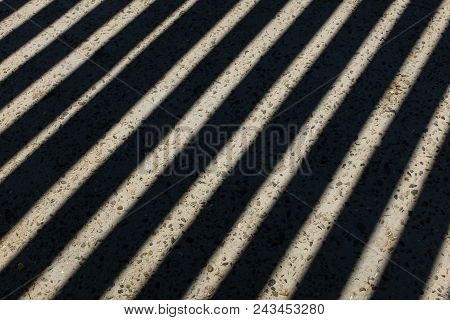 Sunlight Shines Through Wooden Fence And Makes Geometric Stripes Shadows On The Ground. Shadows Of W