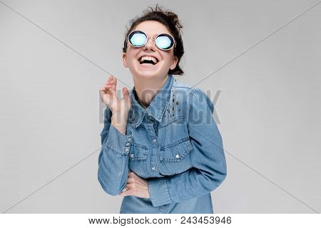 Young Girl In Round Glasses On A Gray Background. Portrait Of A Young Beautiful Girl. Charming Girl 