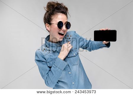 Young Girl In Round Glasses On A Gray Background. Portrait Of A Young Beautiful Girl. Charming Girl 