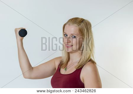 Attractive Young Blond Fitness Woman Working Out With Dumbbell. The Woman Is Smiling At The Camera. 