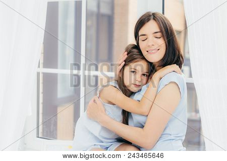 Little Female Child Sits Close To Her Mother, Feels Support And Love Of Her Mum, Pose Together Again