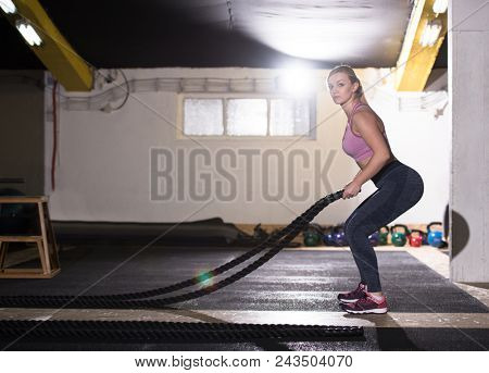 young fit athlete woman working out in functional training gym doing  battle ropes exercise as part of cross fitness training