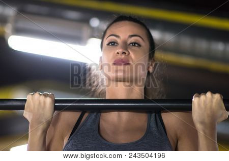 young muscular woman doing pull ups on the horizontal bar as part of Cross fitness Training