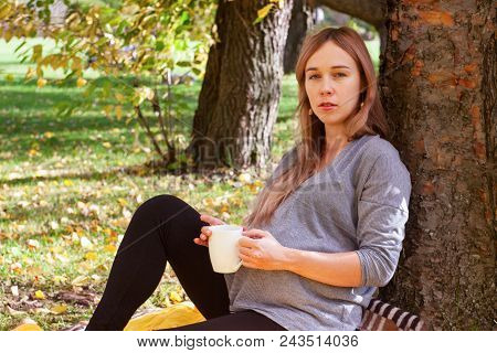 Happy Pregnant Woman Having Hot Drink While Sitting And Reasting In The Autumn Park