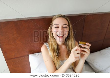 Young Female Person Sitting In Bed With Gold Debit Card And Smling, Sitting In Bed. Concept Of Payme