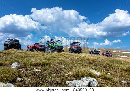 Parked Atv And Utv, Buggies On Mountain Peak With Clouds And Blue Sky In Background.