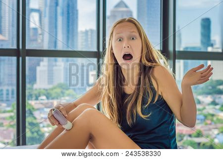 Young Woman Sitin On Bed At Home And Doing Epilation With Epilator On Legsand Is In Pain. On The Bac