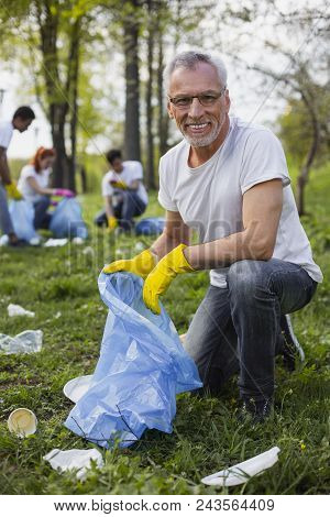Help Nature. Merry Senior Volunteer Dressing In Gloves And Looking At Camera