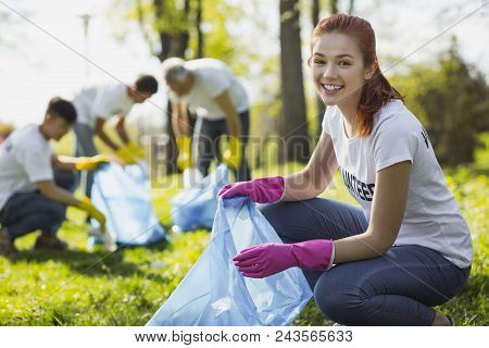 Volunteering In Park. Joyful Female Volunteer Grinning While Gathering Rubbish