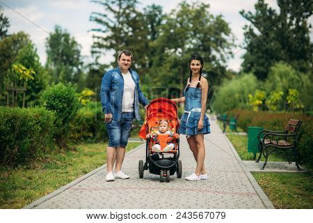 Mom And Dad Walk In The Pakr With A Baby In Baby Buggy.