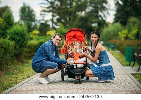Mom And Dad Walk In The Pakr With A Baby In Baby Buggy.