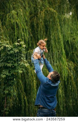 Dad And Daughter Dressed In Jeans Walking In The Pakr And Have Fun.