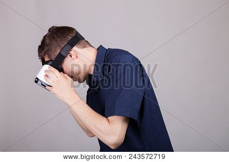Young Man Wearing A Vr Headset On Gray Background In Studio Photo. He Is Experiencing Virtual Realit