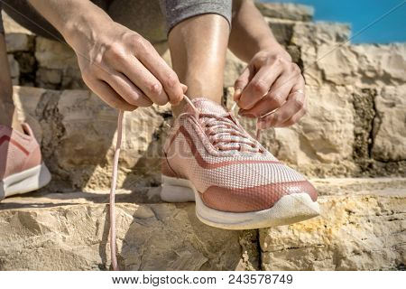 Women runner bootlace on her boot after running in sunny day under sunlight from blue sky on the stone steps.