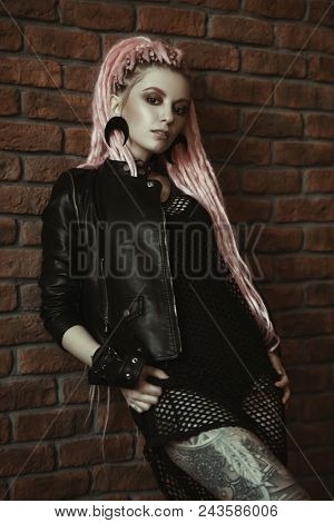 Sexy hipster girl with pink dreadlocks posing by the brick wall. Beauty, fashion.