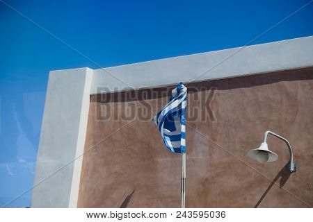 Greece Flag Closed Against A Blue Sky. Typical Mediterranean Urban City Landscape. Santorini Greece