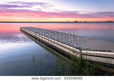 Sunrise Or Sunset On A Fishing Dock Or A Pier With Colorful Clouds Reflecting In The Lake Located In
