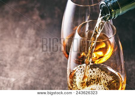 Pouring white wine into the glass against wooden background