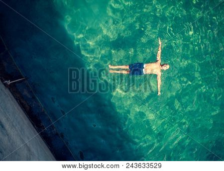 Bird eye view on the man floating in the pool, handsome guy with perfect stong body floating in transparent water, enjoying summer vacation