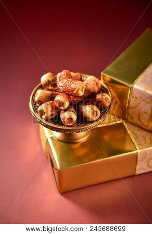 Bowl of dates placed on top of golden gift boxes. Partial view. Dates and golden gift box.