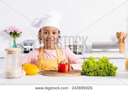 Smiling African American Kid In Apron And Chef Hat Preparing Vegetables On Kitchen