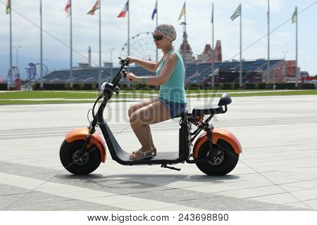 SOCHI, RUSSIA - JUL 09, 2017: woman on scooter on background of bowl of Olympic flame Firebird