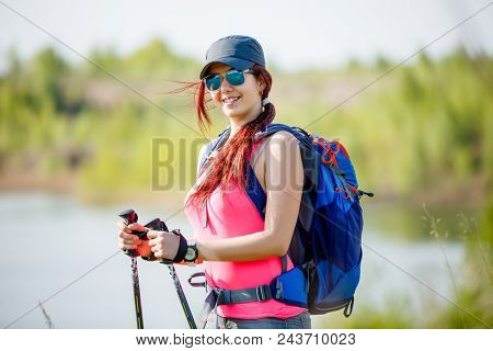 Photo of sports girl with walking sticks on background of lake and green vegetation