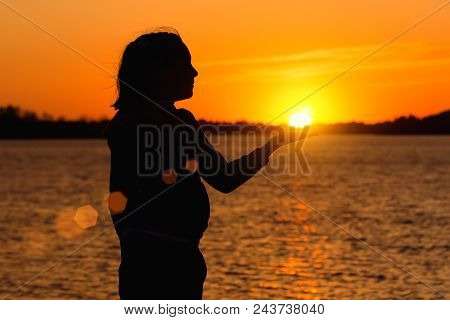 Silhouette Of A Girl On The Background Of The Evening Sun Red Sunset, Keeps The Sun In His Hand