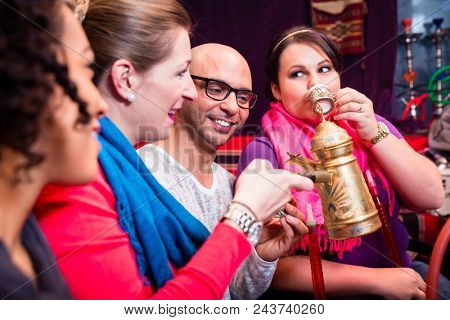 Group of friends smoking hookah and drinking coffee in shisha lounge enjoying themselves