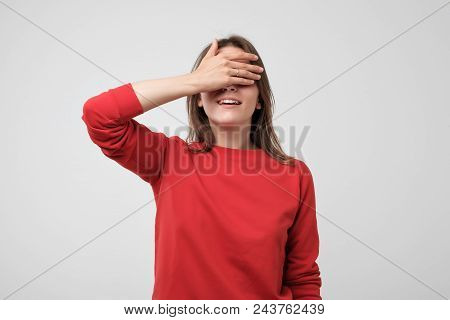 Portrait Of Pretty Woman In Red Sweater Closing Her Eyes With Palm. She Is Waiting For Surprise Or G