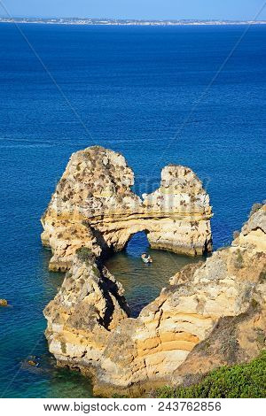 Elevated View Of The Coastline And A Natural Arch In The Ocean And A Boat To The Centre, Praia Da Do