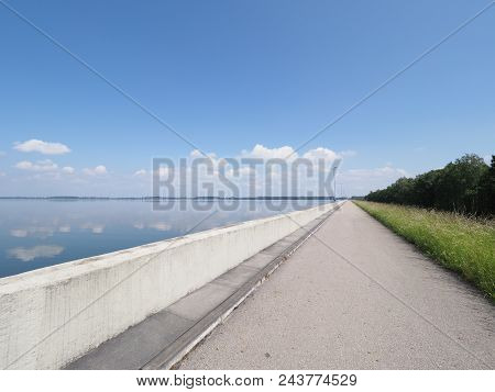 Walkway With Lamps On Barrage At Countryside Landscapes Of Lake, Grassy Field, Forest On European Ar