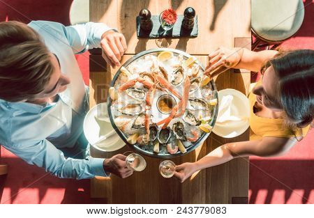 High-angle view of a happy young couple toasting with champagne during romantic dinner with fresh seafood at a trendy restaurant