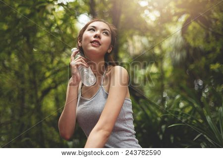 Relaxed Asian Beautiful Woman In Grey Vest Shirt Holding A Bottle Of Water At Green Forest Backgroun