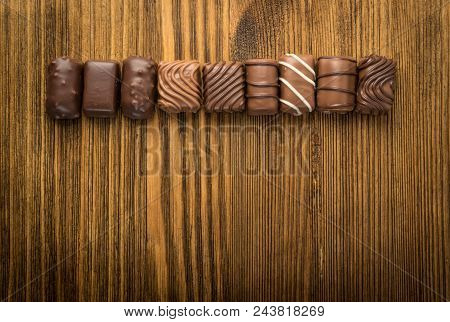Beautiful Creative Chocolate Sweets On Natural Wooden Table Background. Line Of Chocolates Top View 