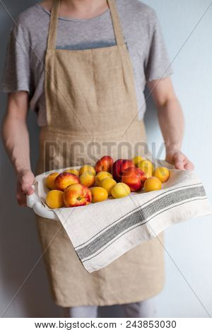 A Man Is Holding A Tray Fukk Of Fresh Apricots And Peaches From The Garden.