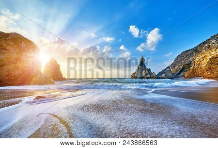 Portugal Ursa Beach at atlantic coast of Atlantic Ocean with rocks and sunset sun waves and foam at sand of coastline picturesque landscape panorama.