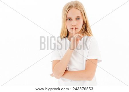 Mystery young blonde girl in casual clothes showing silence gesture and looking at the cameraa over white background