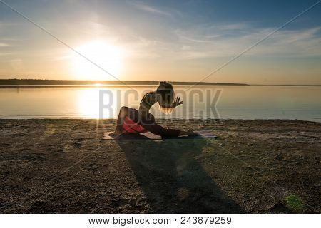 Silhouette Woman On The Beach At Sunset Doing Yoga Asana. Morning Natural Stretch Warm-up Training