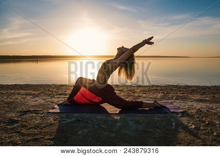 Silhouette Woman On The Beach At Sunset Doing Yoga Asana. Morning Natural Stretch Warm-up Training